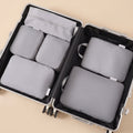 Stowmade compression packing cubes, the six-piece grey set arranged inside an open suitcase on a warm sand background