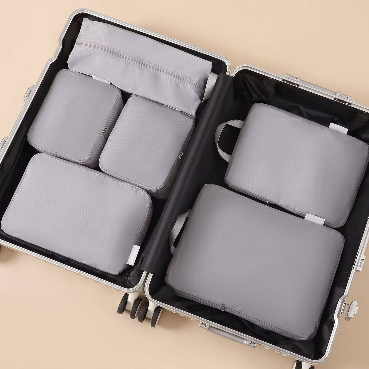 Stowmade compression packing cubes, the six-piece grey set arranged inside an open suitcase on a warm sand background