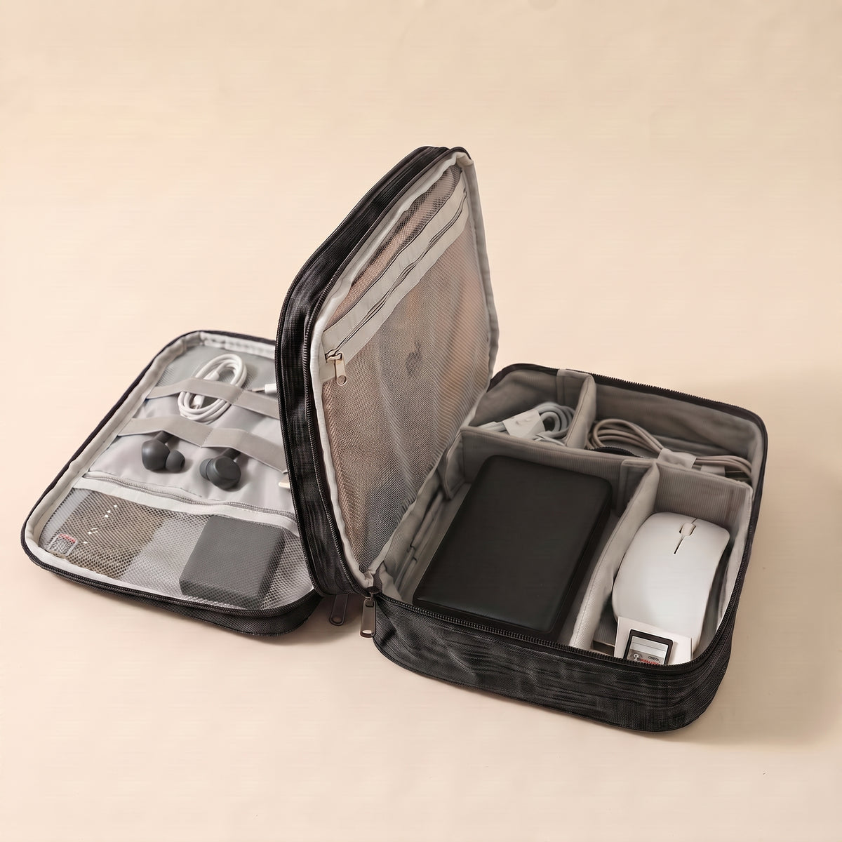 Stowmade tech organiser in black, open on a warm sand background with cables, a power bank and a mouse in labelled compartments #Black