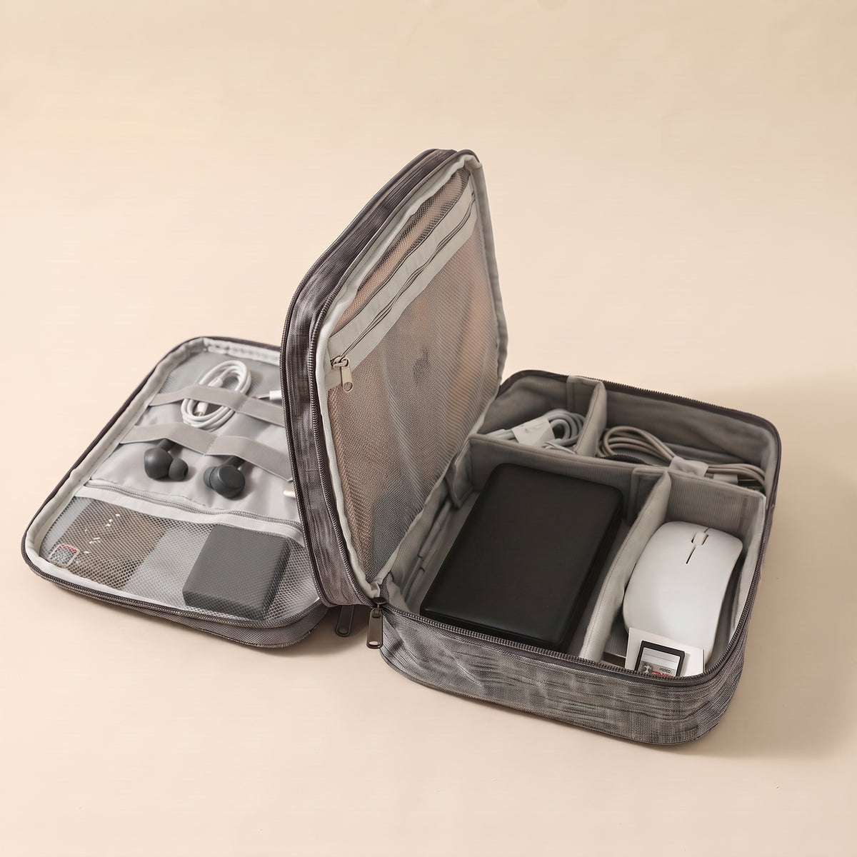 Stowmade tech organiser in grey, open on a warm sand background with cables, a power bank, a mouse and earbuds in labelled compartments #Gray