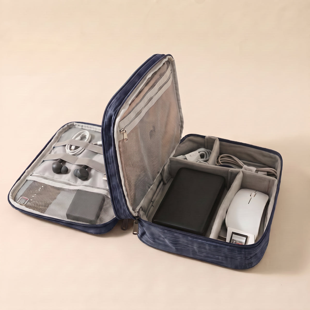 Stowmade tech organiser in navy blue, open on a warm sand background with cables, a power bank and a mouse in labelled compartments #NavyBlue